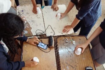Estudiantes jugando con vasos en el aula sobre pupitres unidos como mesa