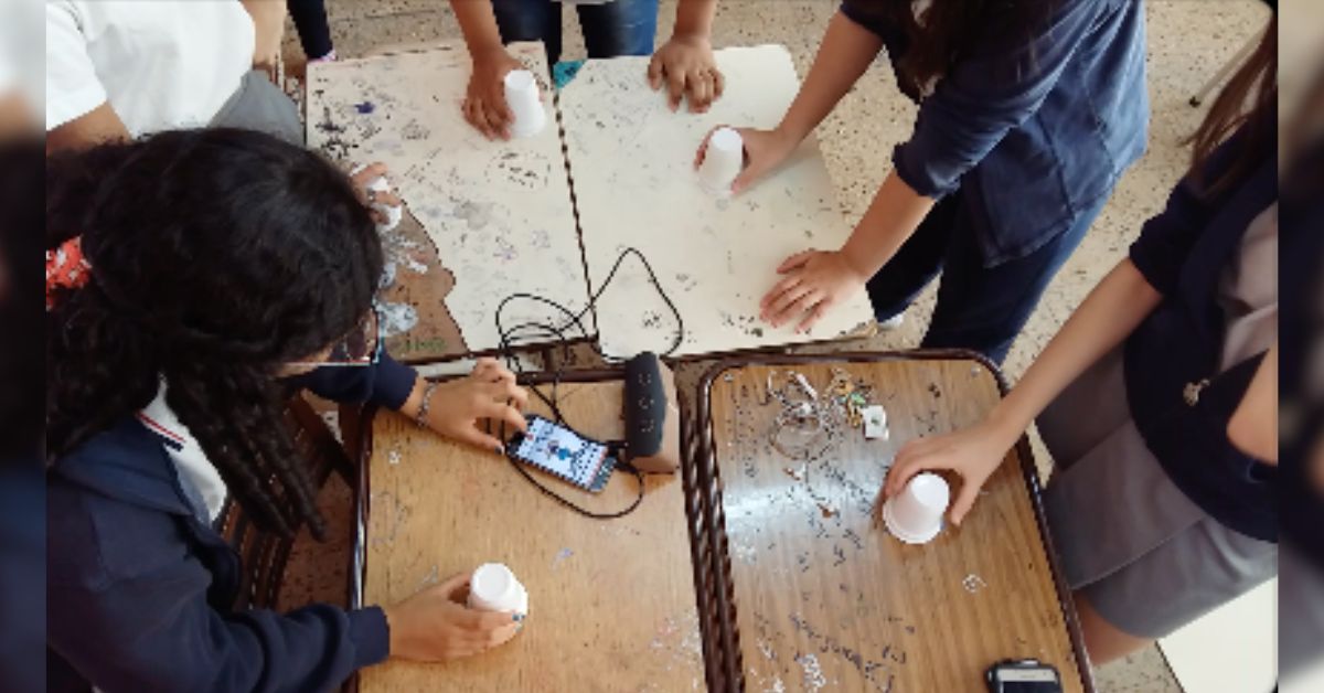 Estudiantes jugando con vasos en el aula sobre pupitres unidos como mesa